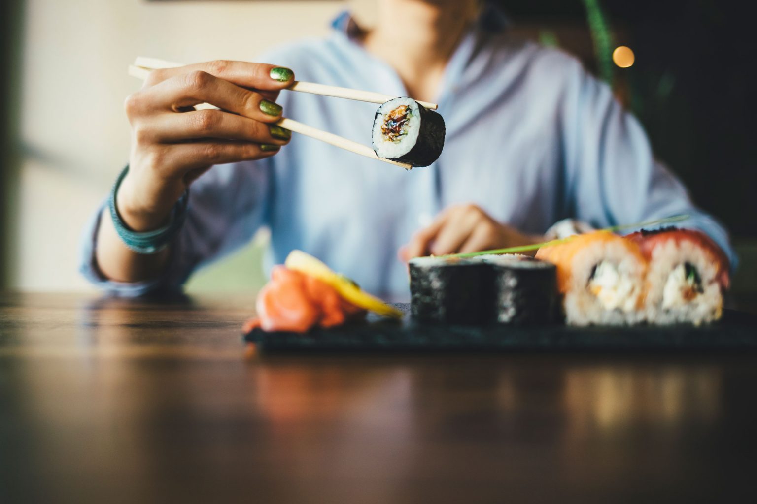 A person holding an individual roll of sushi with a pair of chopsticks.