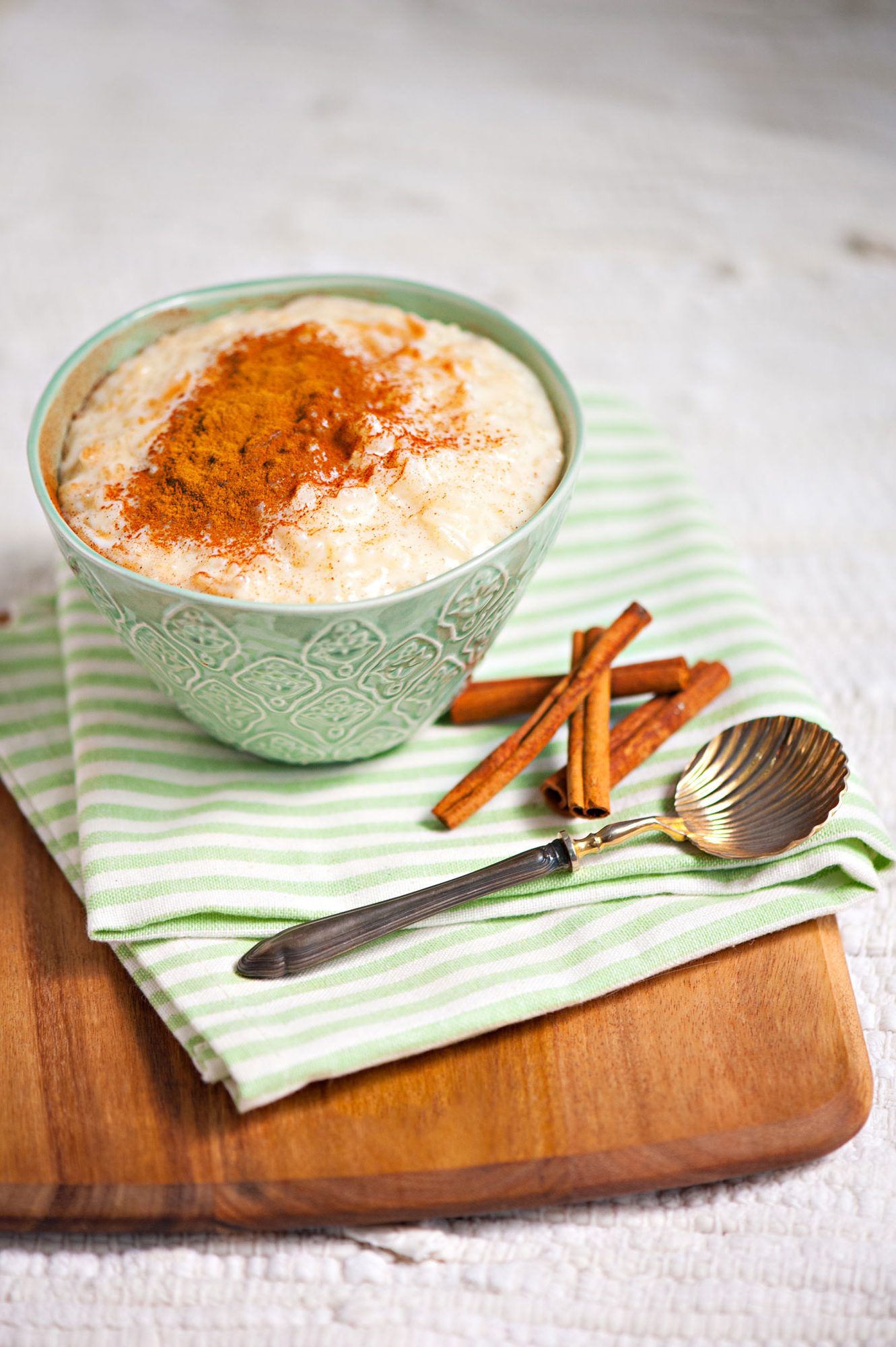 Rice pudding sprinkled with cinnamon in a intricate green bowl.