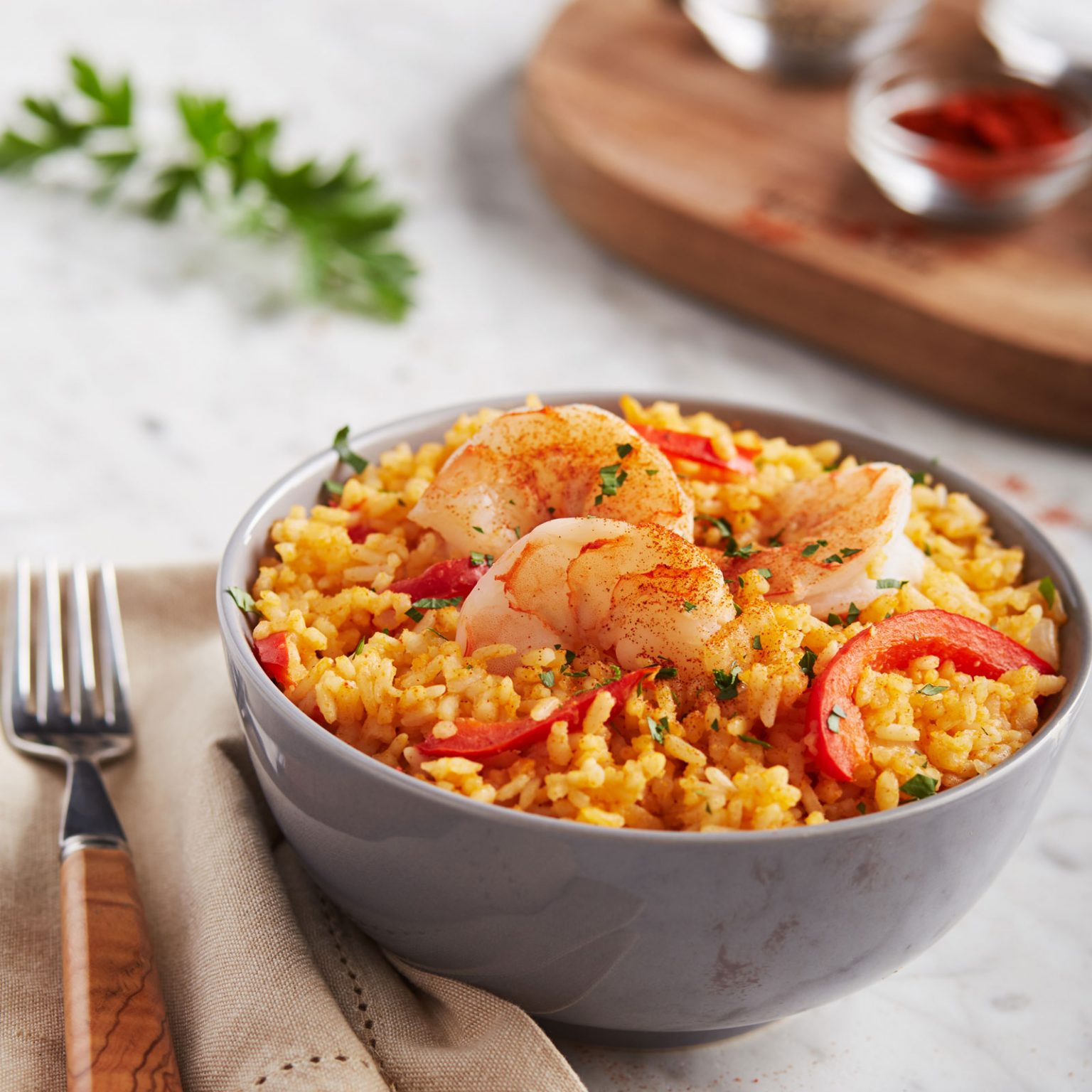 A gray bowl filled with Mexican rice with red bell pepper and cooked shrimps.
