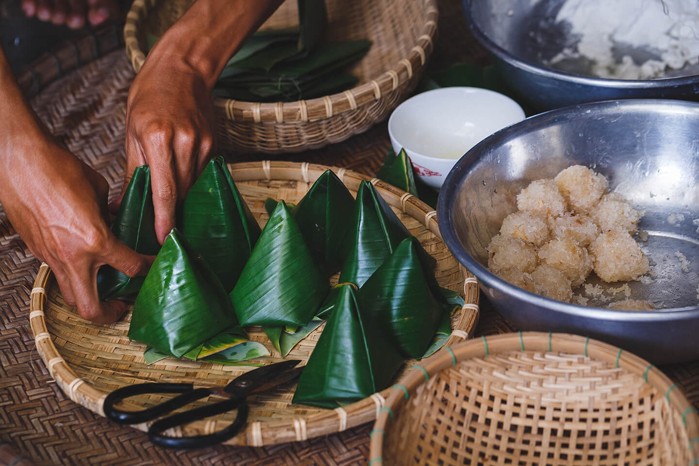 Bundles of food wrapped in vibrant bamboo leaves in a large woven basket.