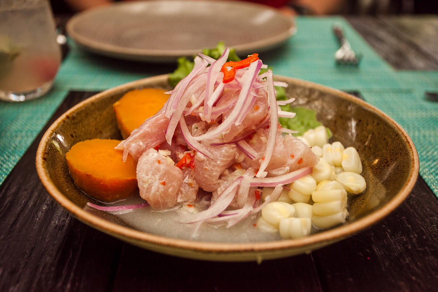 A dark bowl filled with freshly made ceviche topped with sliced red onions.