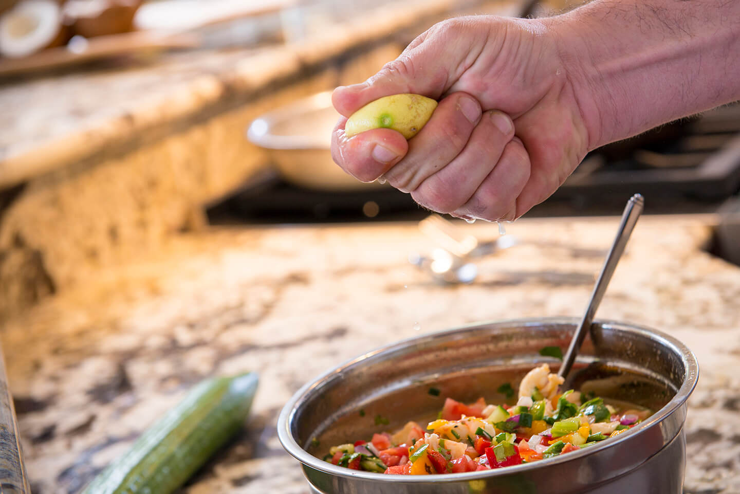 A person squeezing lemon into a silver bowl of ceviche.