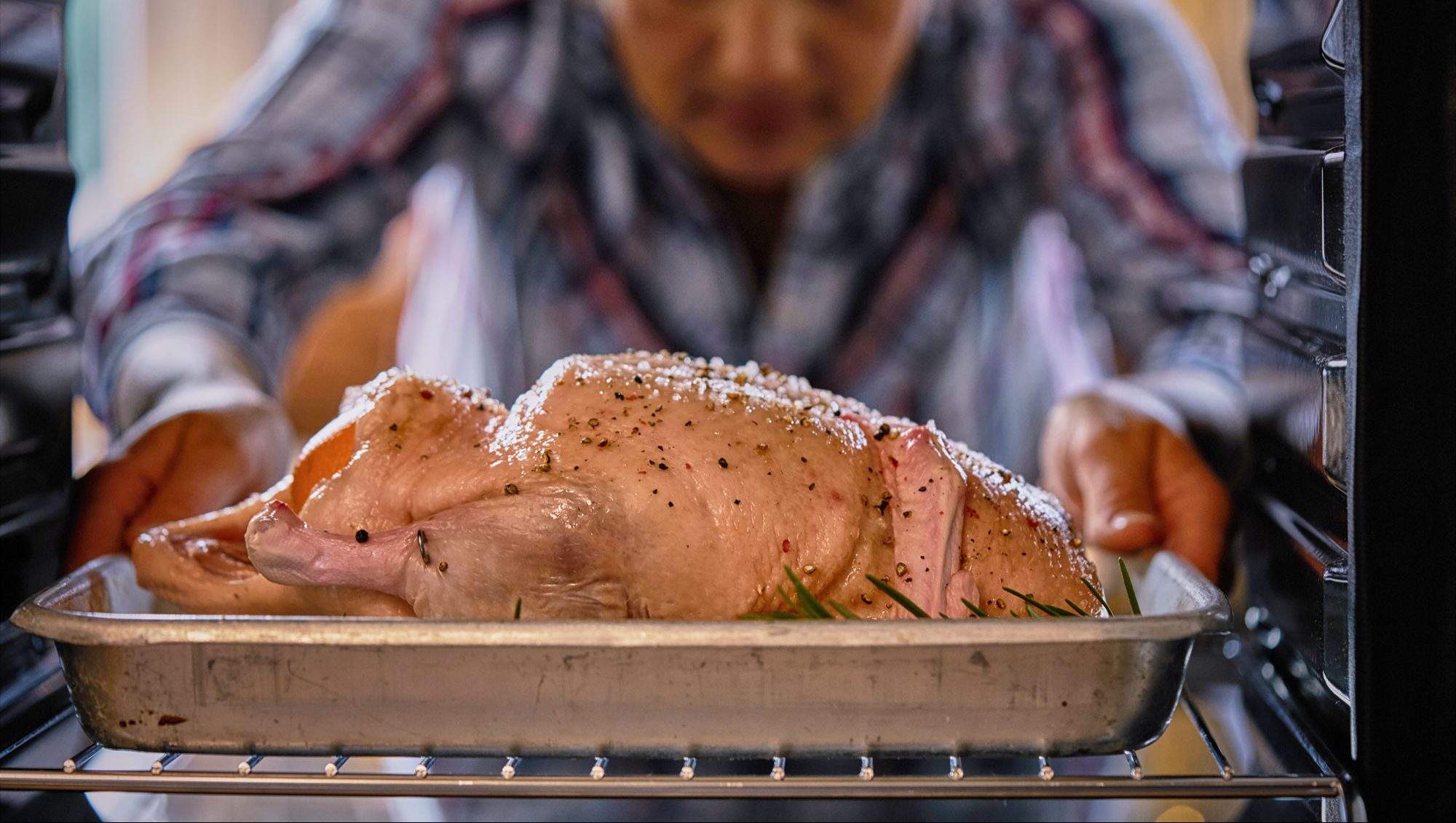 A person placing a whole duck in the oven to be roasted.