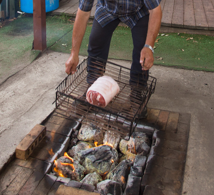 A man preparing Maori hangi: food wrapped in wet cloth in a metal basket.
