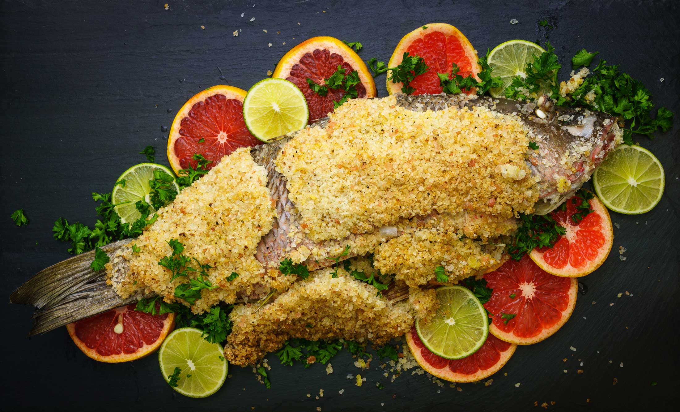A salt-crusted sea bass resting atop thinly sliced citruses.