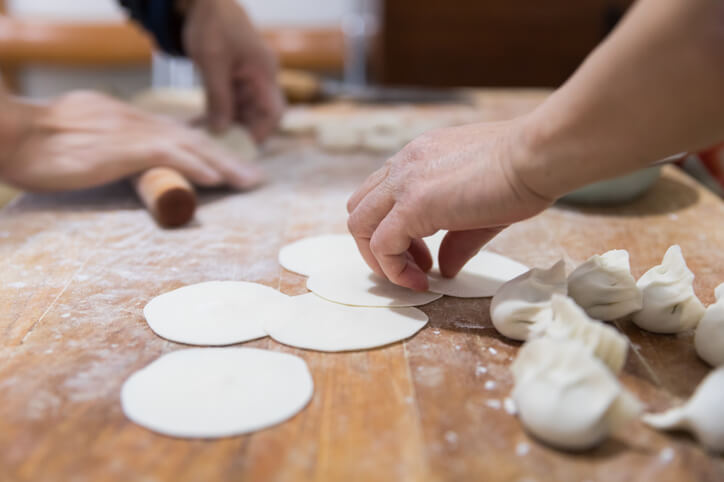 Two people working together at a kitchen table preparing dumplings from scratch.