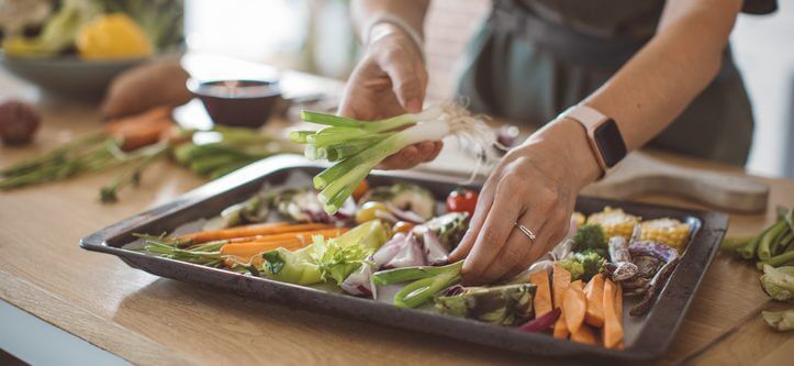 A woman neatly placing green onions on a baking sheet filled with chopped vegetables.