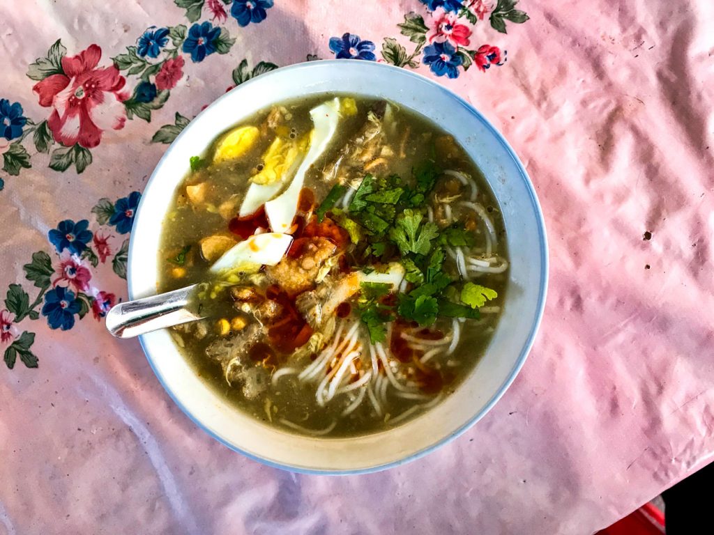 A bowl of mohinga on a floral table cloth.