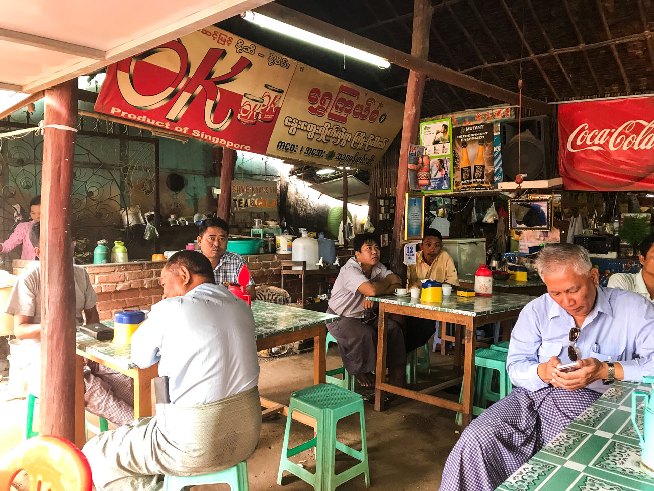 A local eatery in Myanmar filled with guests sitting on stools.