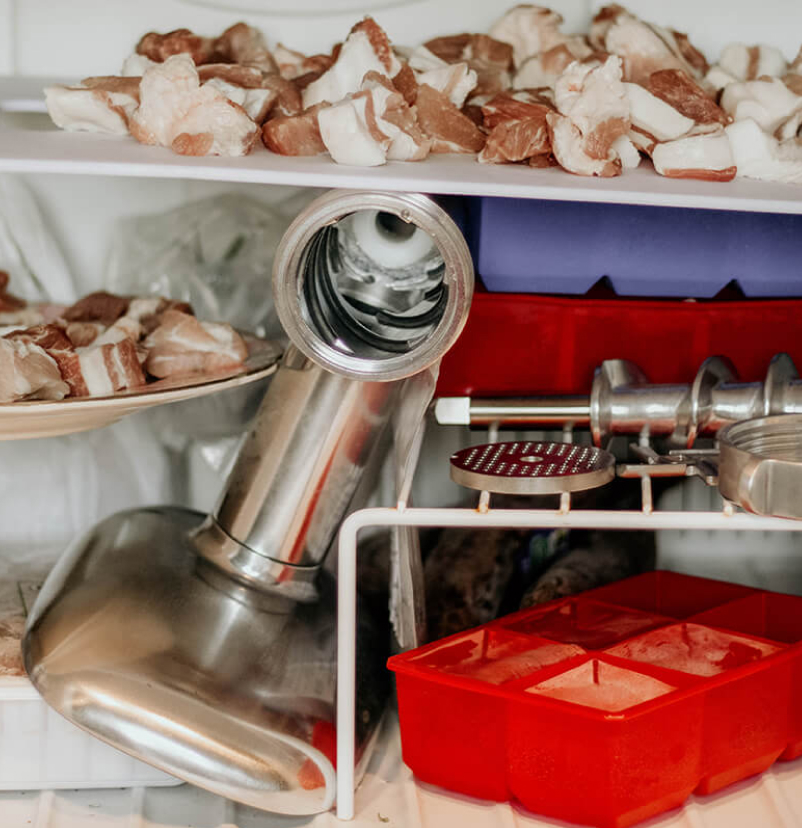 A freezer filled with uncovered meat and a KitchenAid® food grinder.