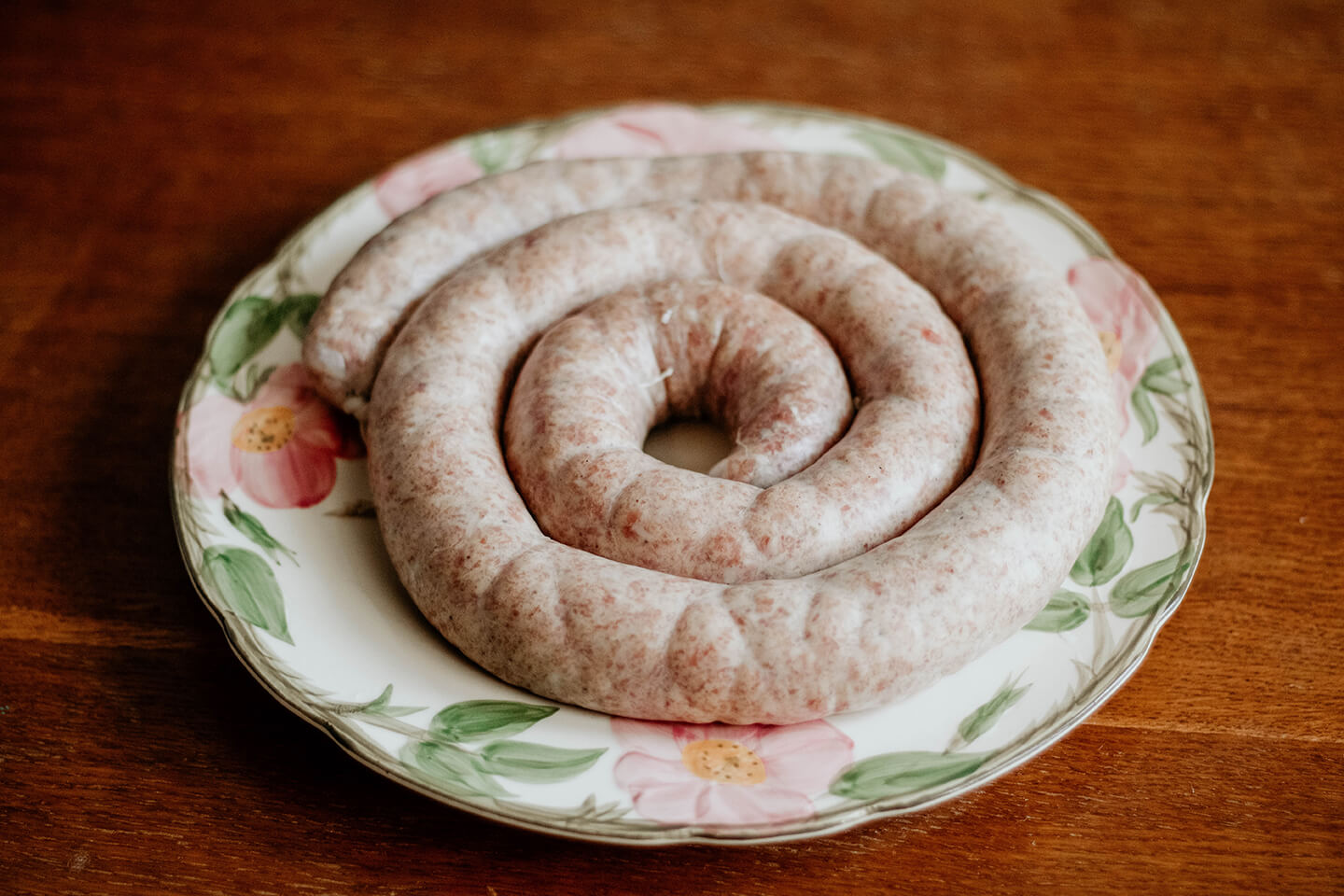 Freshly made sausage resting on a floral china plate.