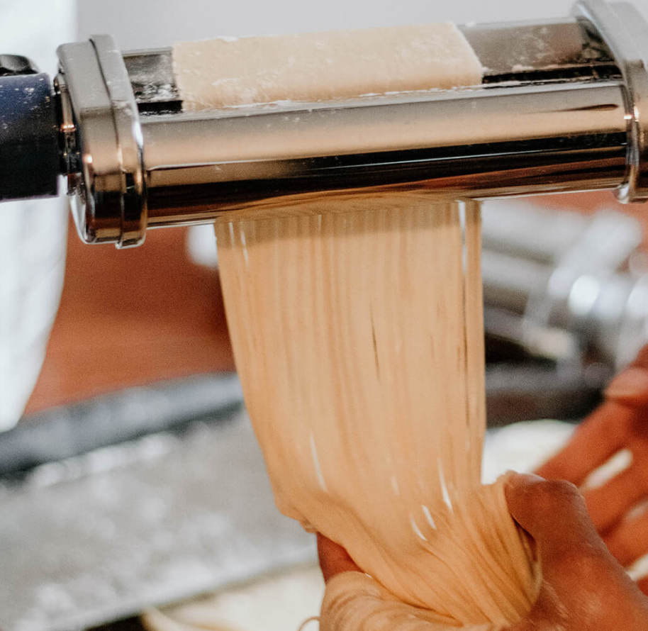 A person making homemade pasta with a KitchenAid® pasta roller attachment.