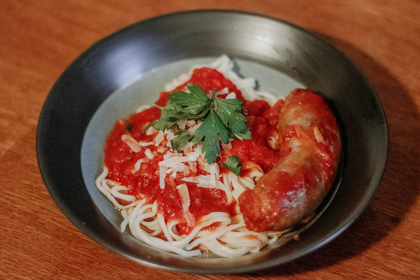 A bowl of freshly made pasta served with sauce and cooked sausage.