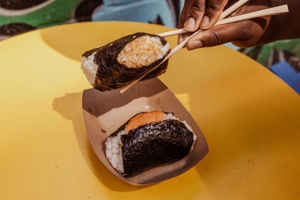 A person holding a rice ball in between two chopsticks.