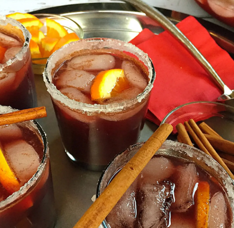 A cocktail with a salted rim, cinnamon sticks and orange slices.