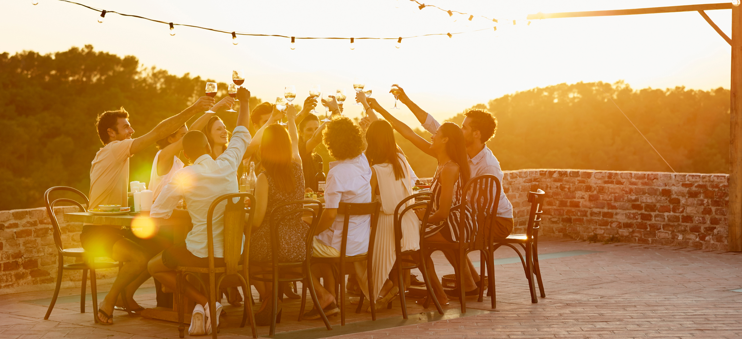A group of people raising their glasses in a toast at sunset.