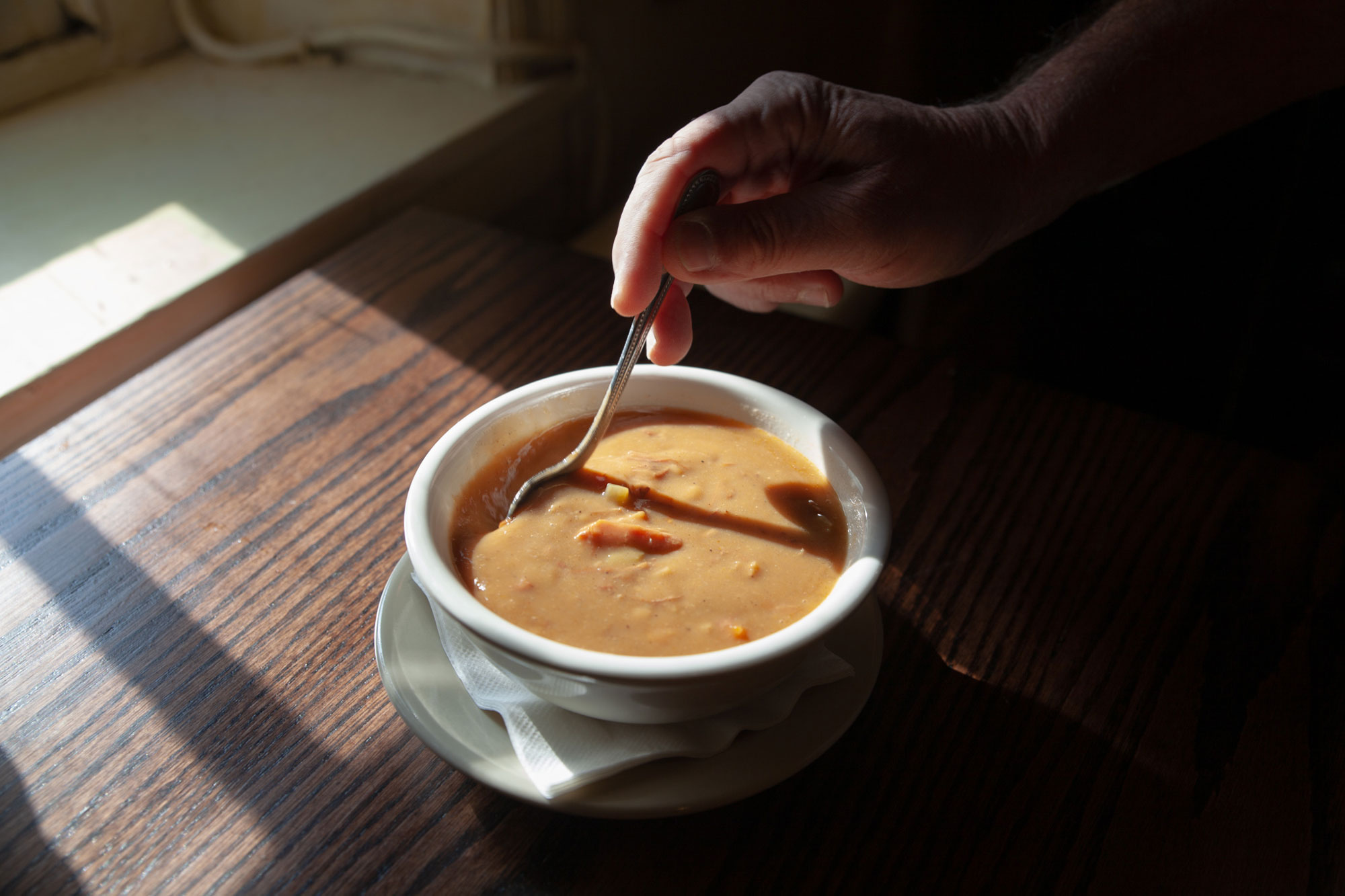 A person stirring a spoon in a small bowl of snapper soup.