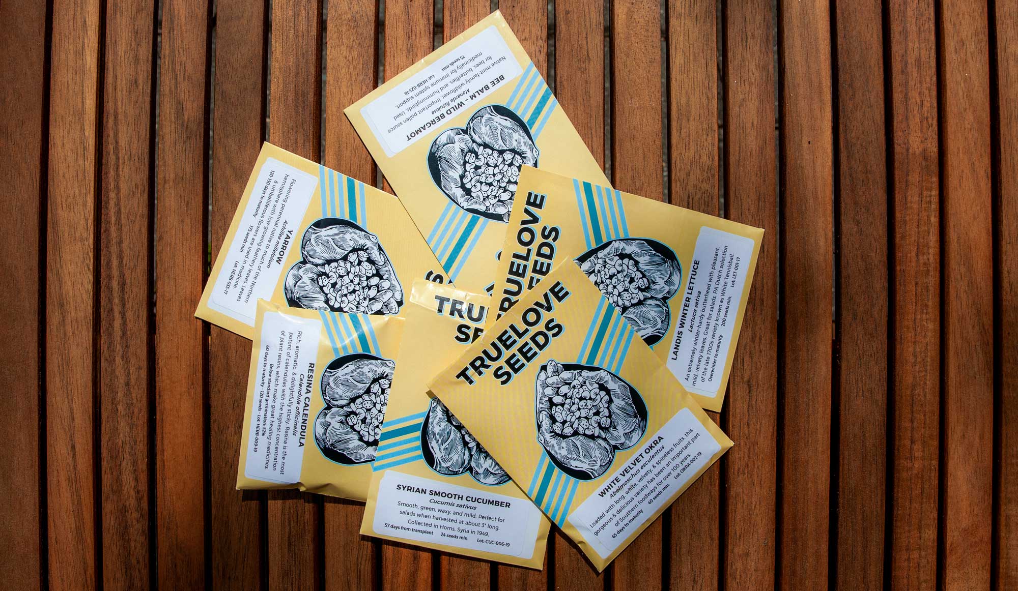 Six individual packets of True Love Seeds resting on a wooden table.