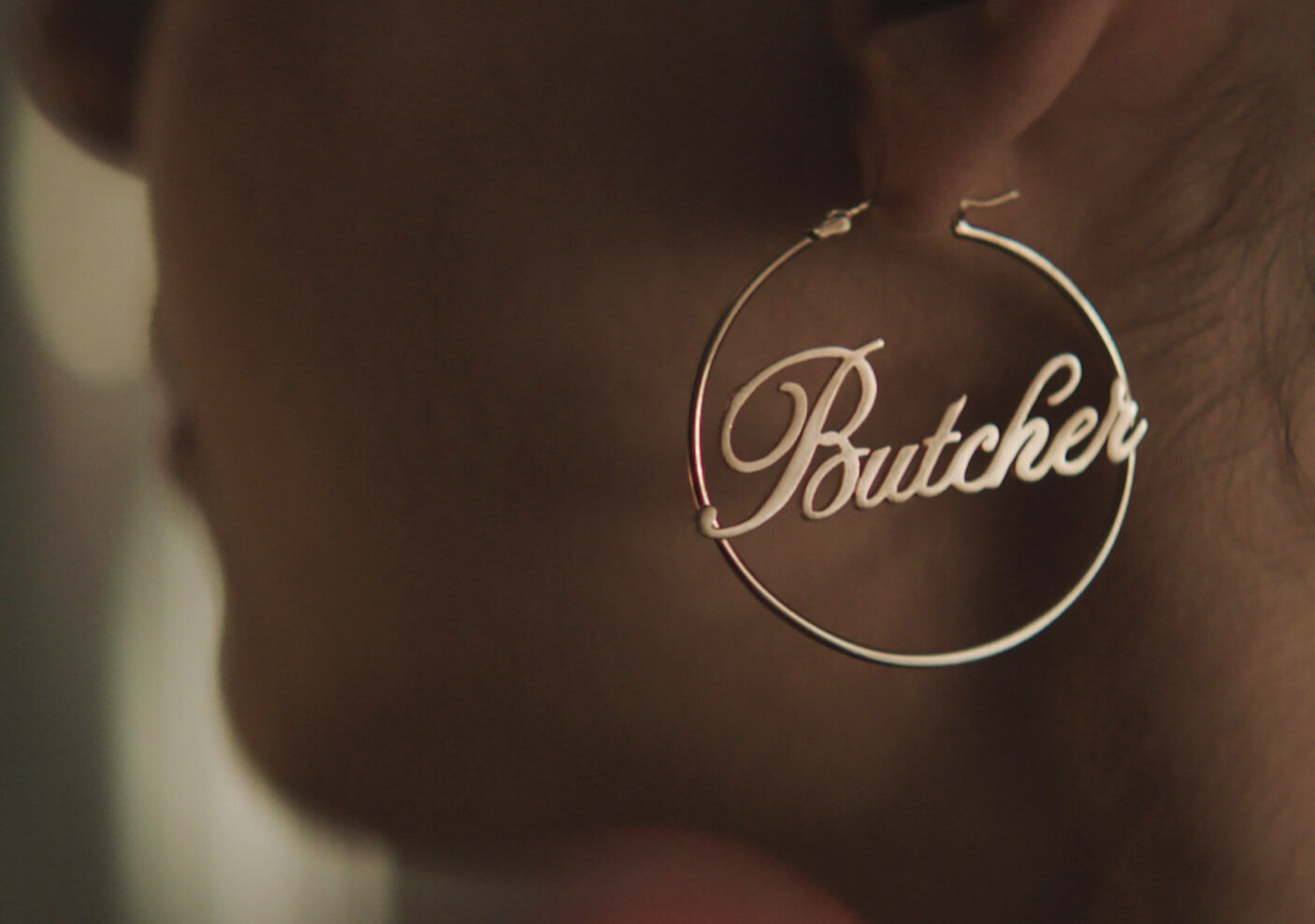 A golden hoop earring with a cursive Butcher in center.