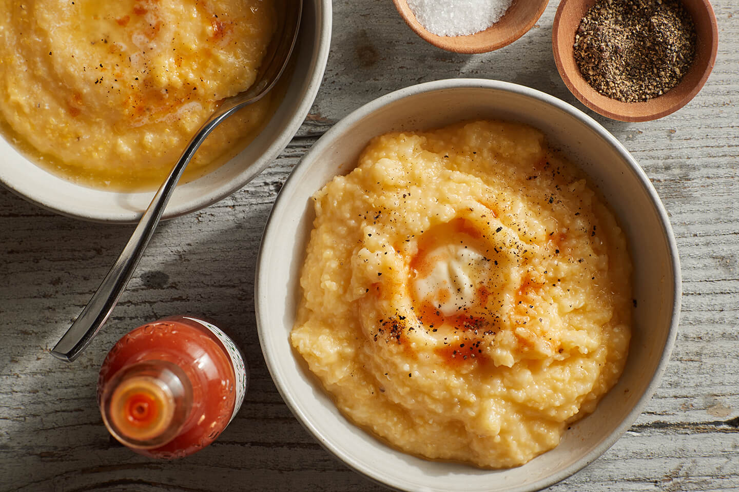 A bowl of creamy grits topped with hot sauce.