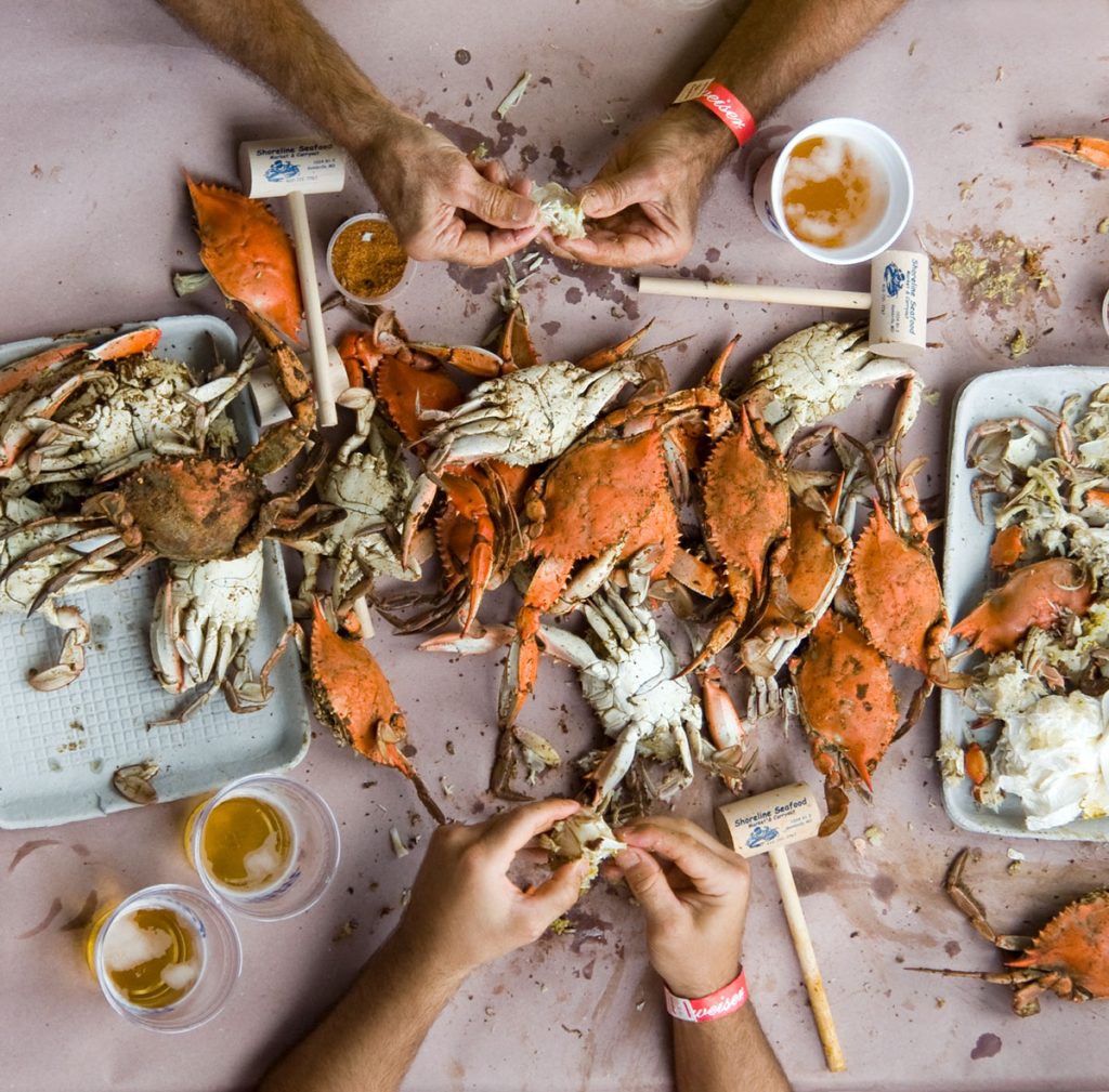 A crab boil feast strewn about a table as a person enjoys.