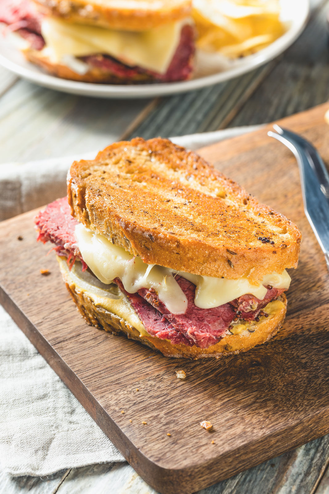 A corned beef sandwich with melted cheese on a wooden cutting board.