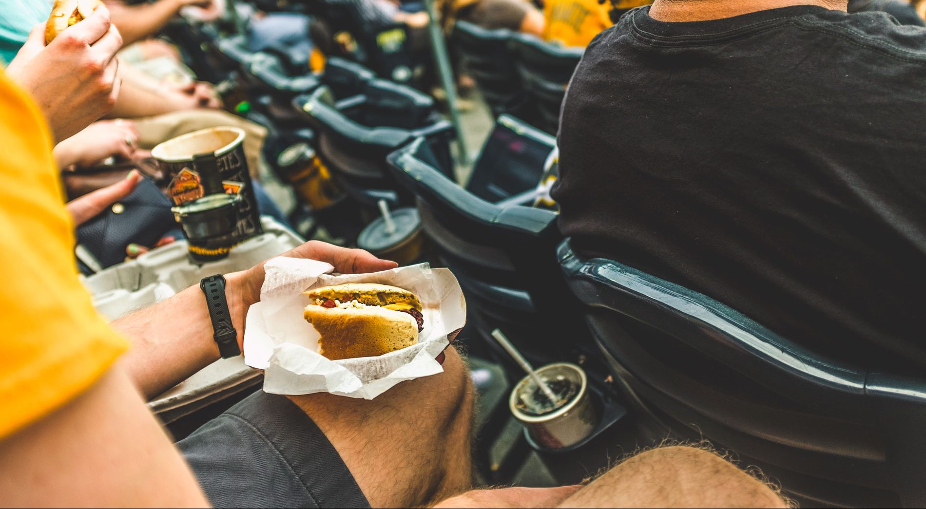 A person eating oversized hot dog in a baseball stadium.
