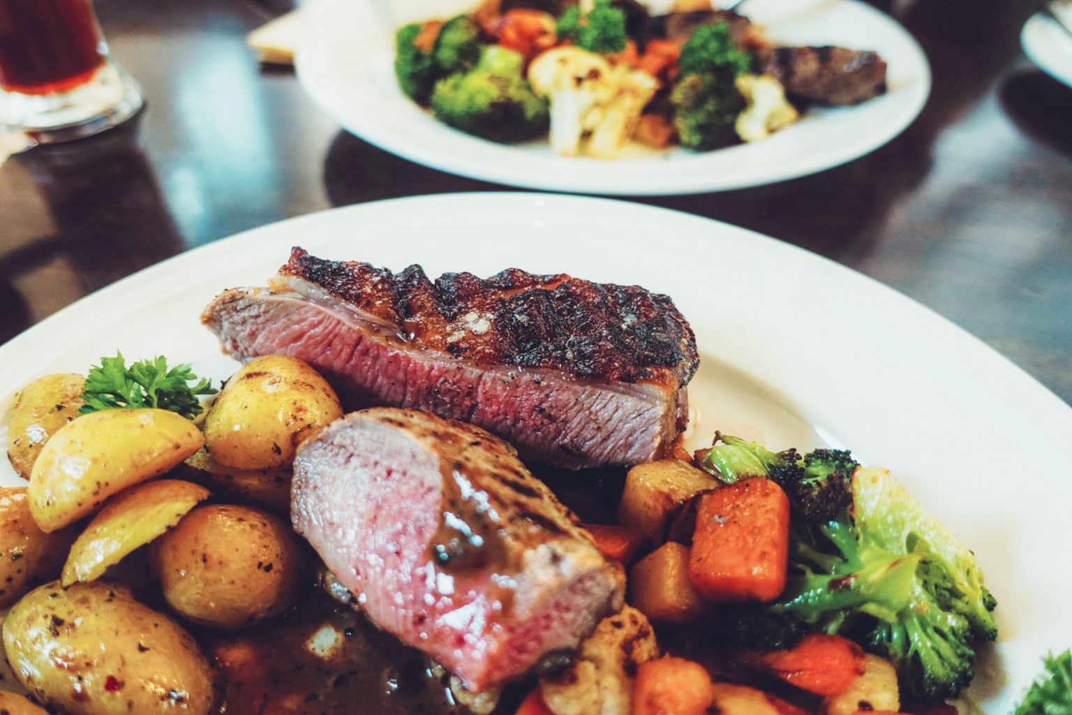 A white plate filled with grilled meat, potatoes and other vegetables.