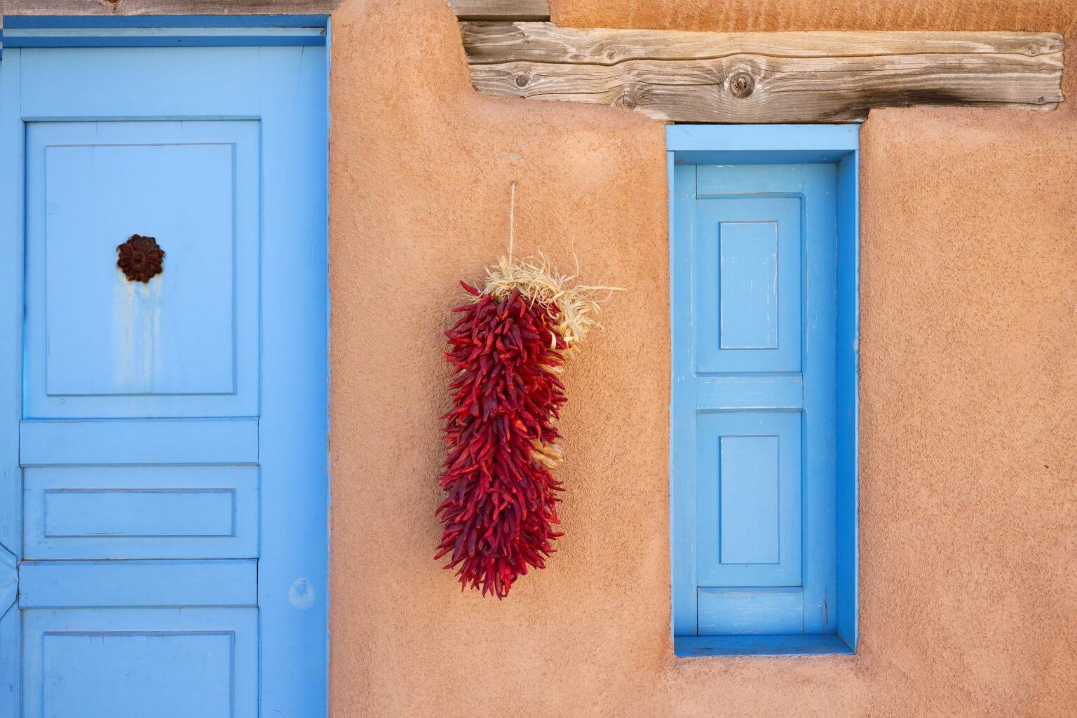 An adobe constructed household adorned with a batch of hanging dried, red chile peppers.