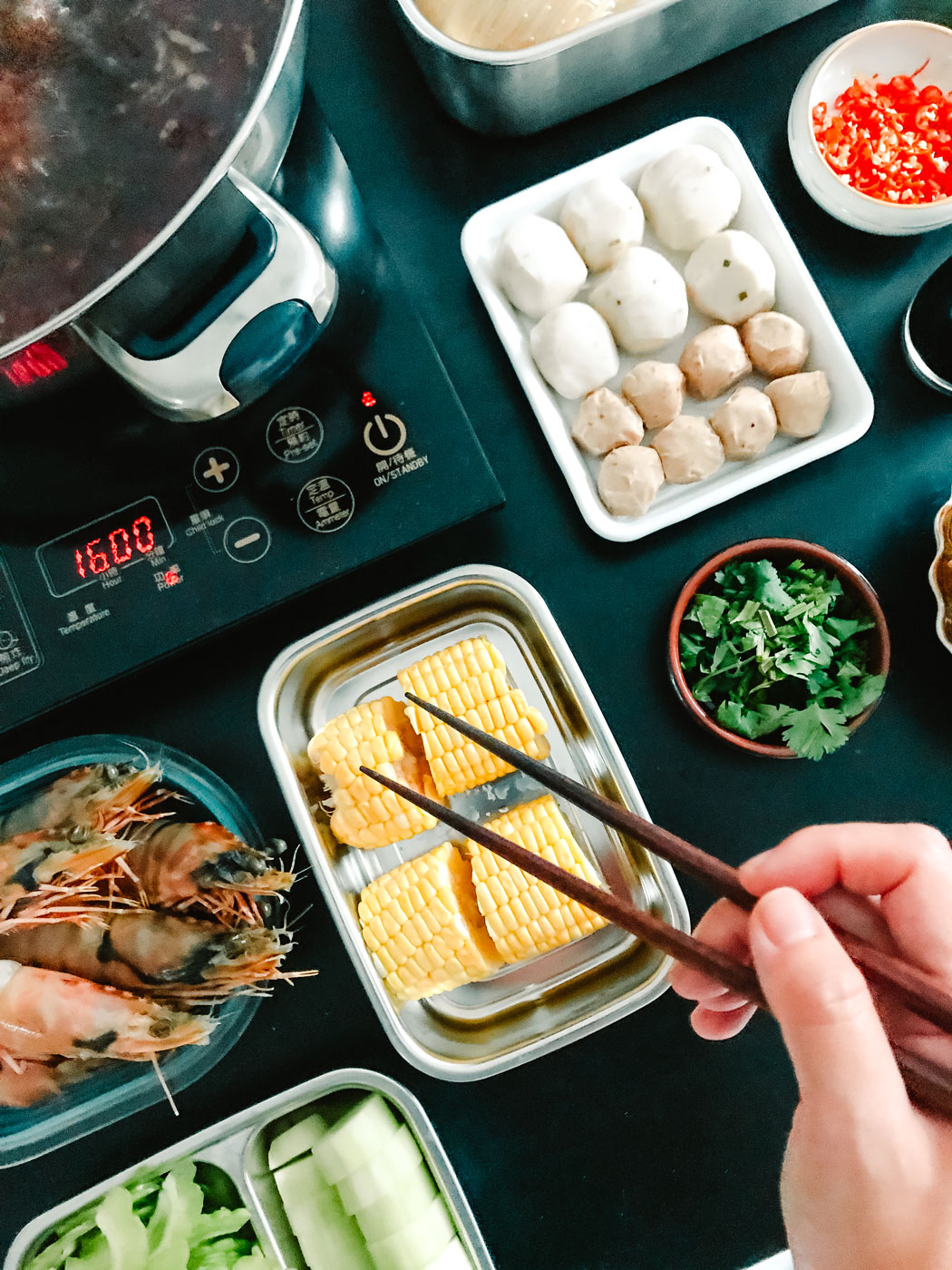 A black table with trays of raw corn, prawns and other ingredients.