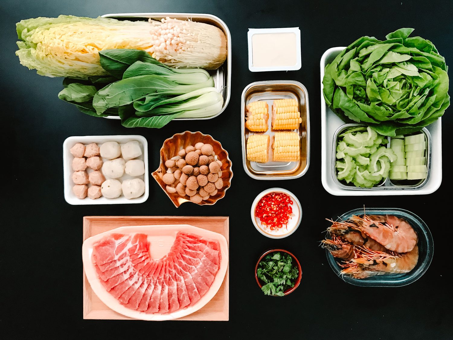 A black table with small trays of raw vegetables, meats and other ingredients.