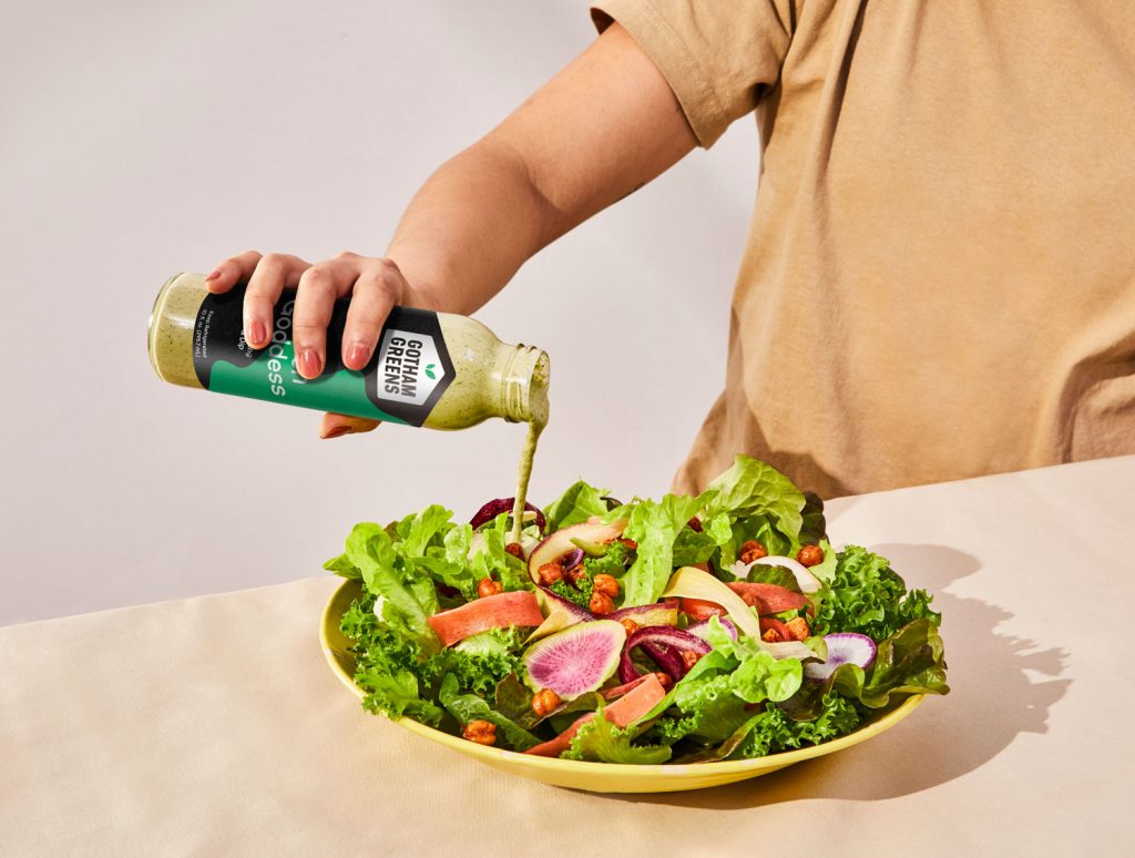 A person pouring dressing on a salad.