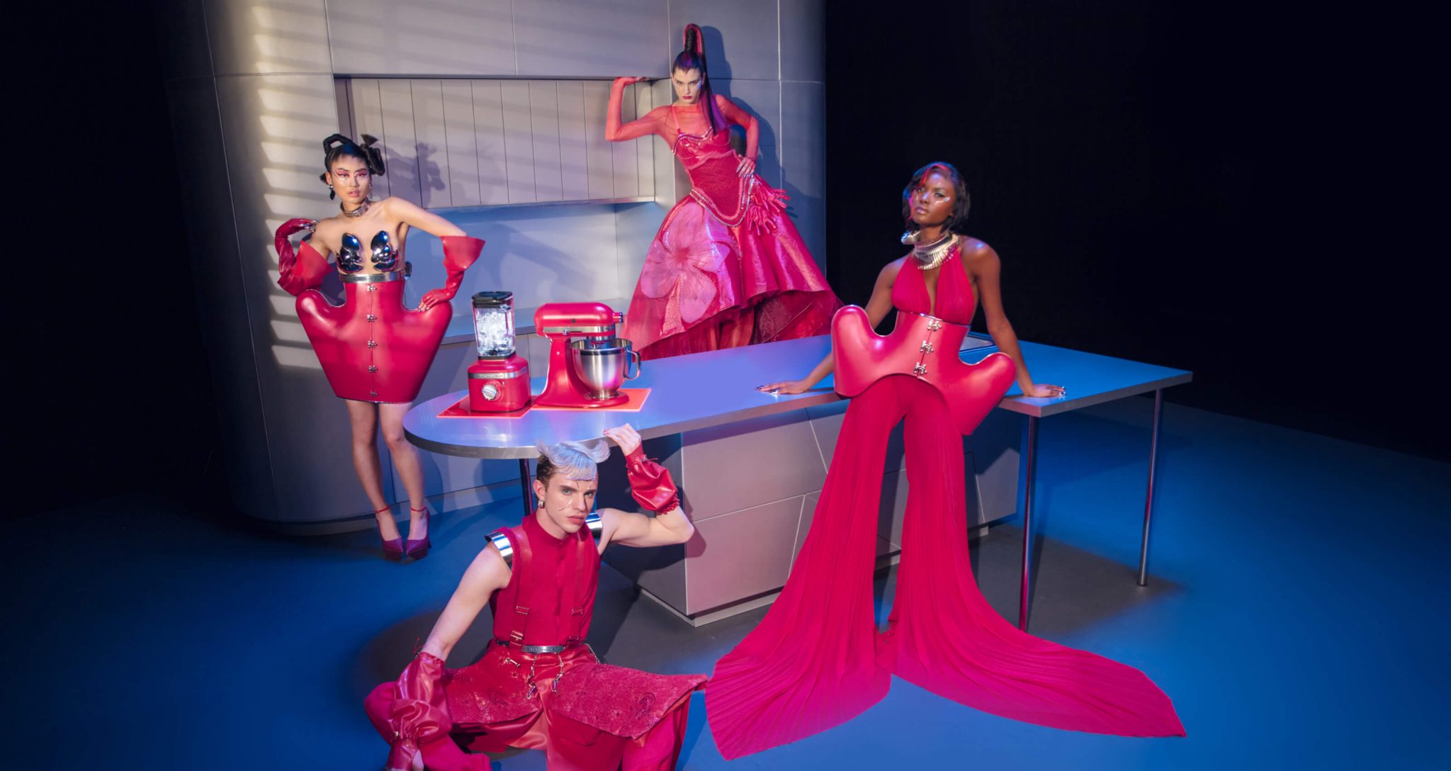 Four models dressed in Hibiscus Collection designs in a chrome kitchen with the Hibiscus stand mixer and blender.
