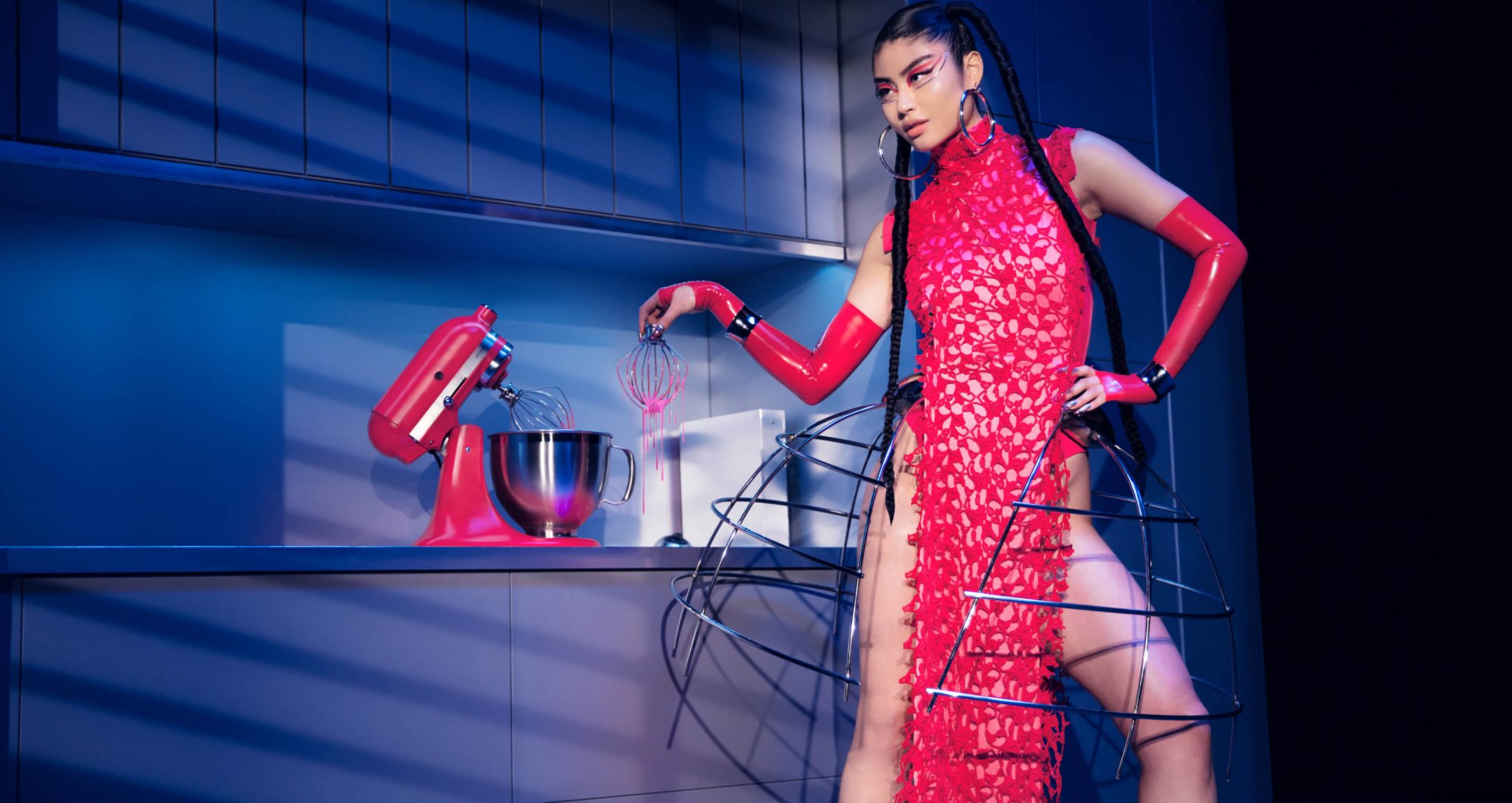 A model dressed in Marta Del Rio’s New York Fashion Week Collection posing in a kitchen with the KitchenAid® Artisan® Series Stand Mixer in Hibiscus.