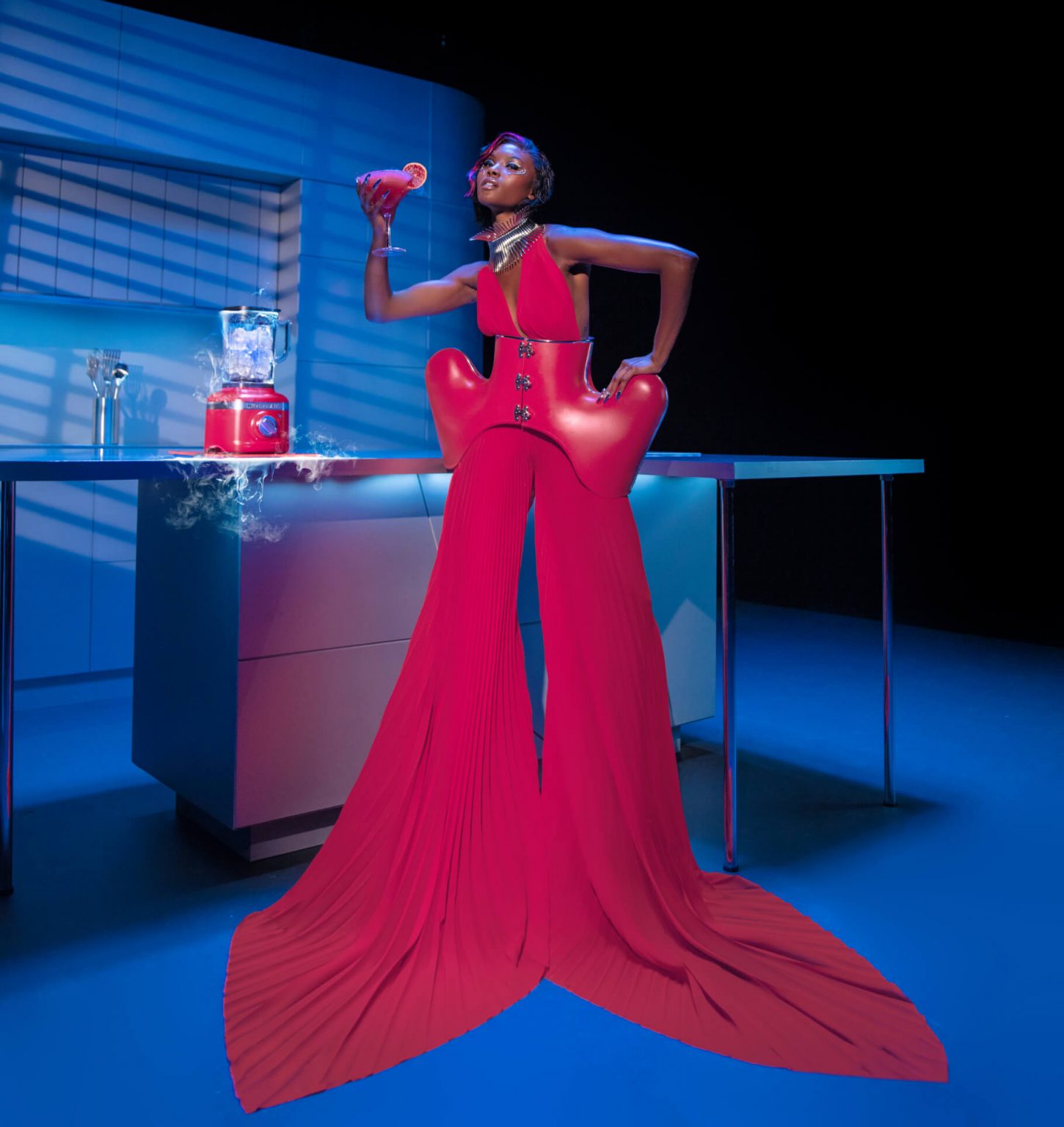 A model dressed in one of Marta Del Rio’s Hibiscus Collection looks posing with the blender and a mixed drink.