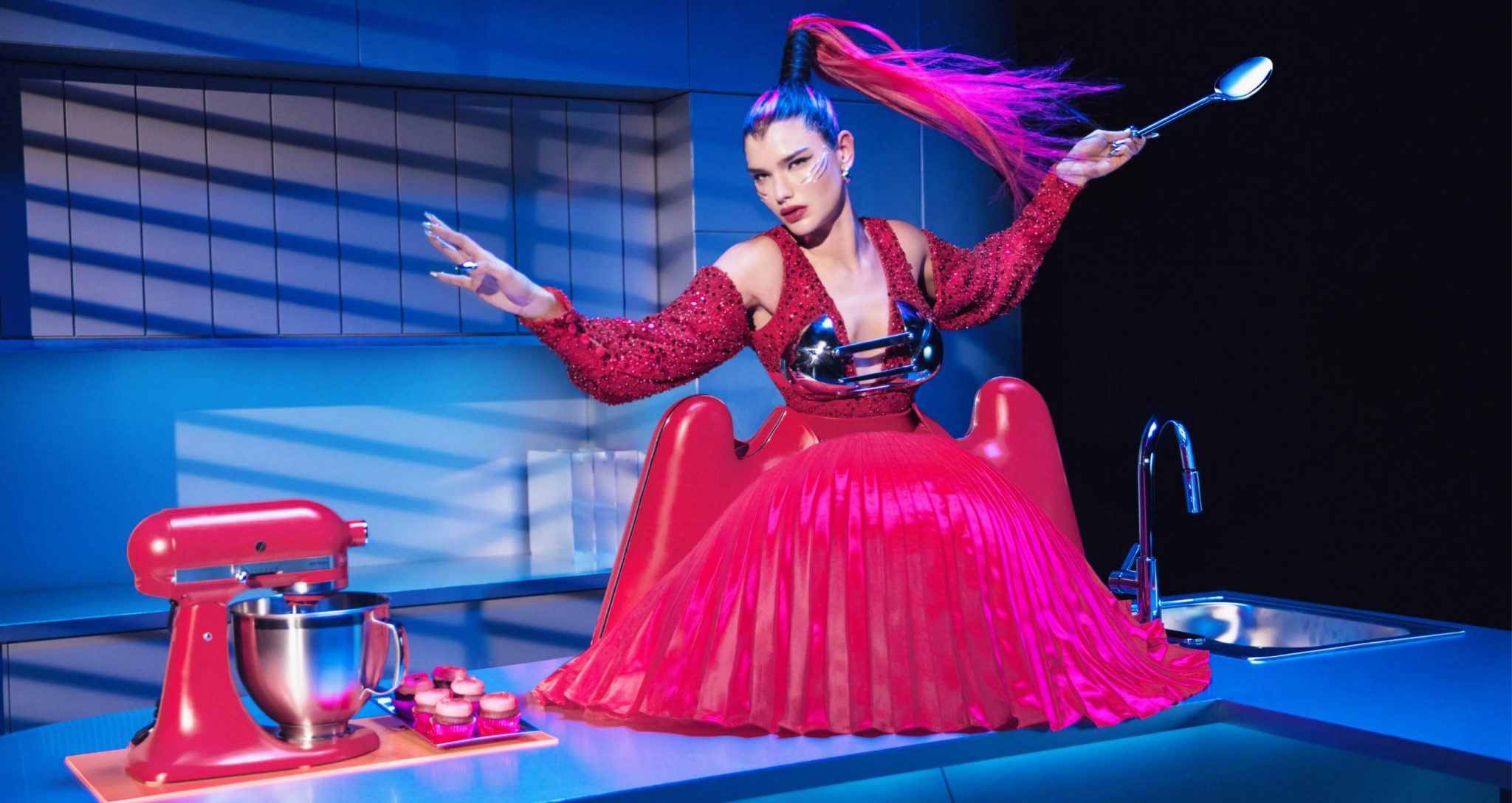 A model standing on the counter of the kitchen wearing Look Four near the Artisan® Series Stand Mixer and decorated fuchsia cupcakes and a detail shot of the cupcake liner-inspired skirt.