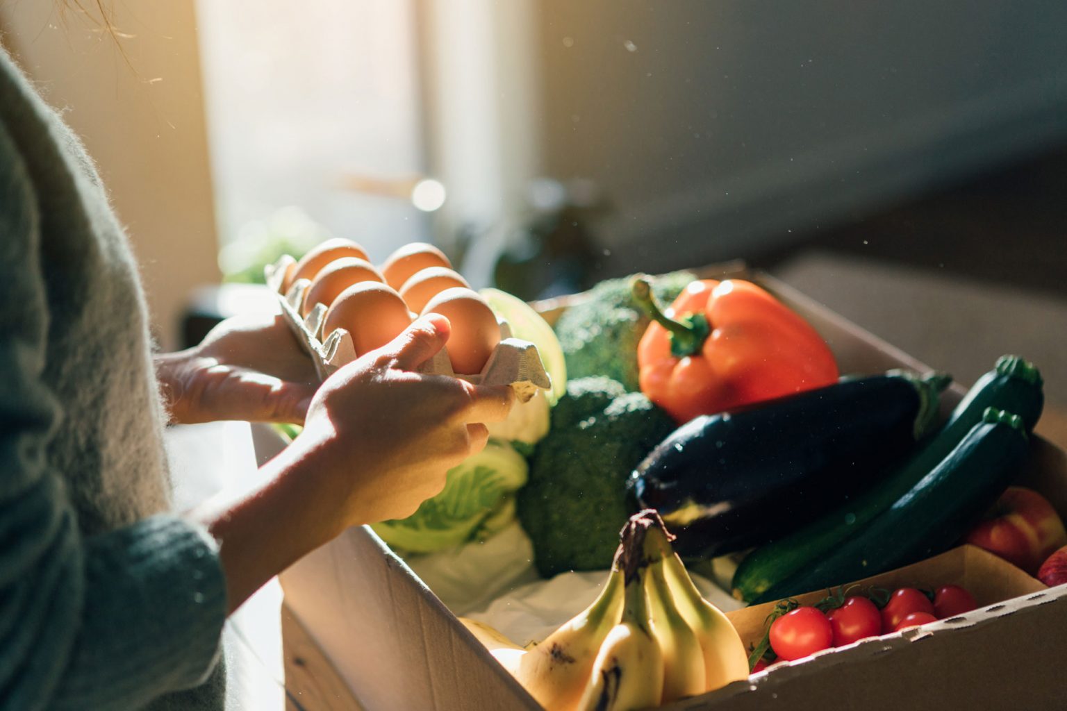 A person sorting through a carton of eggs and fresh produce.