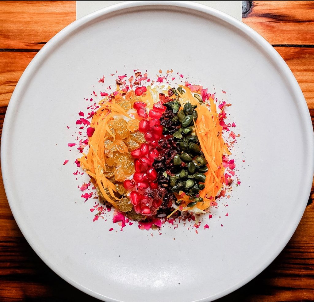 Pomegranate seeds, dried fruits, nuts and other delicacies served on a white plate.