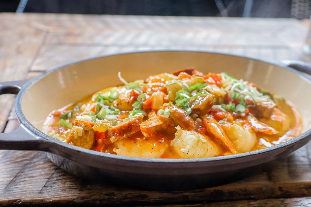 An oval dish filled with steaming cajun shrimp and grits.