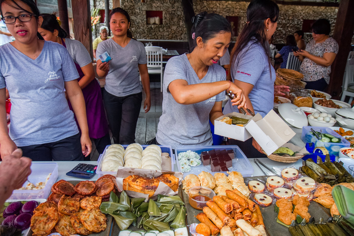 Women gently packing Indonesian desserts into a white carryout box.