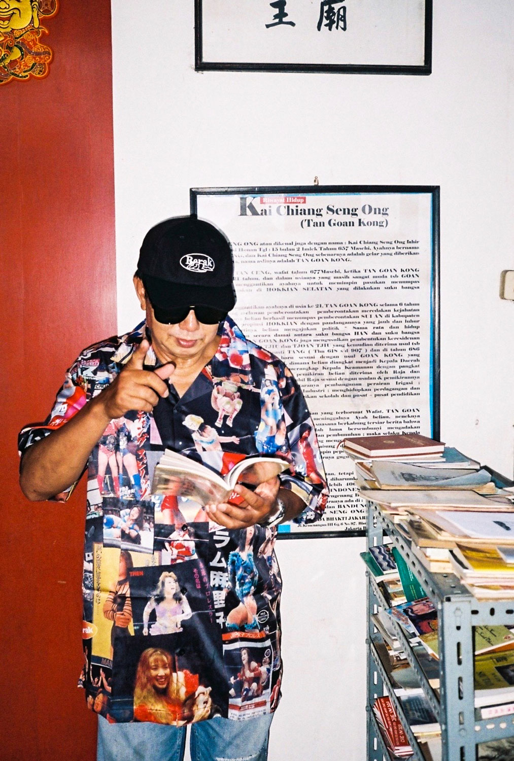Paulus Supomo in a retro shirt and sunglasses reading a magazine.