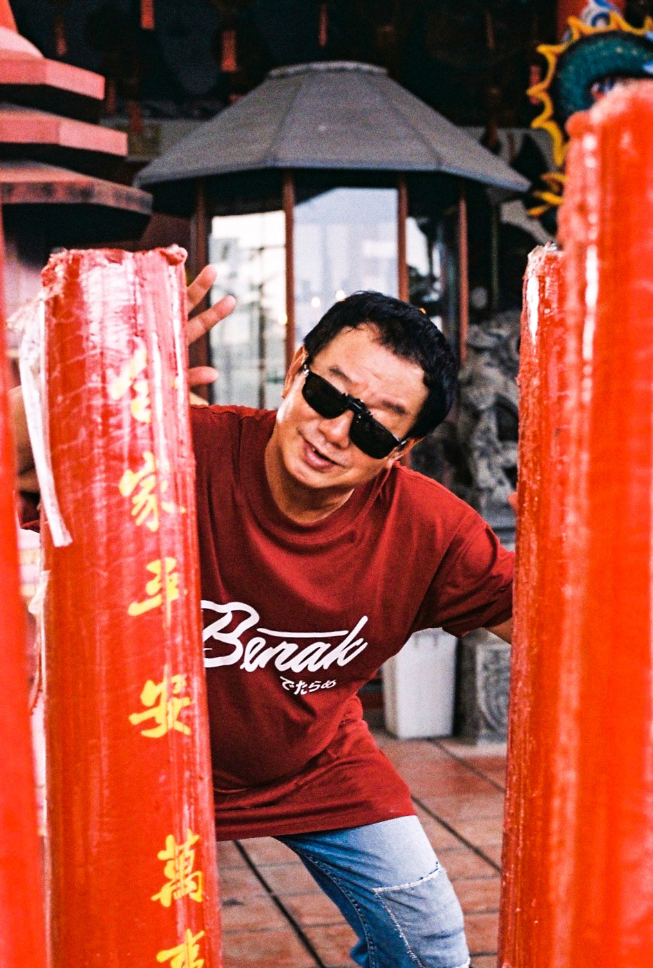 Paulus Supomo in sunglasses posing behind red pillar with yellow Chinese lettering on the street.