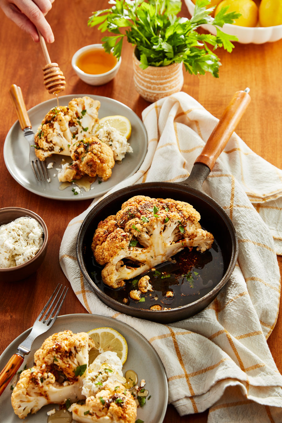 A skillet of roasted cauliflower surrounded by served plates.