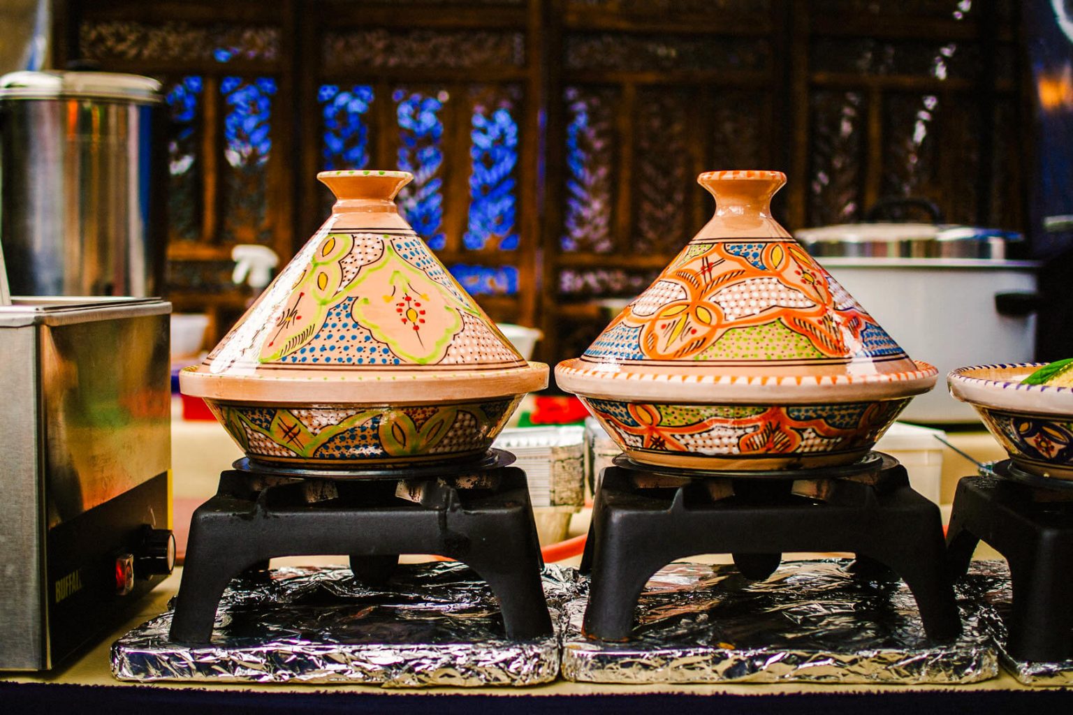 Two colorful, beautifully painted tagine pots set on top of black cooking grates.