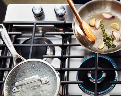 A boiling pot and pan of cauliflower on a gas stove.