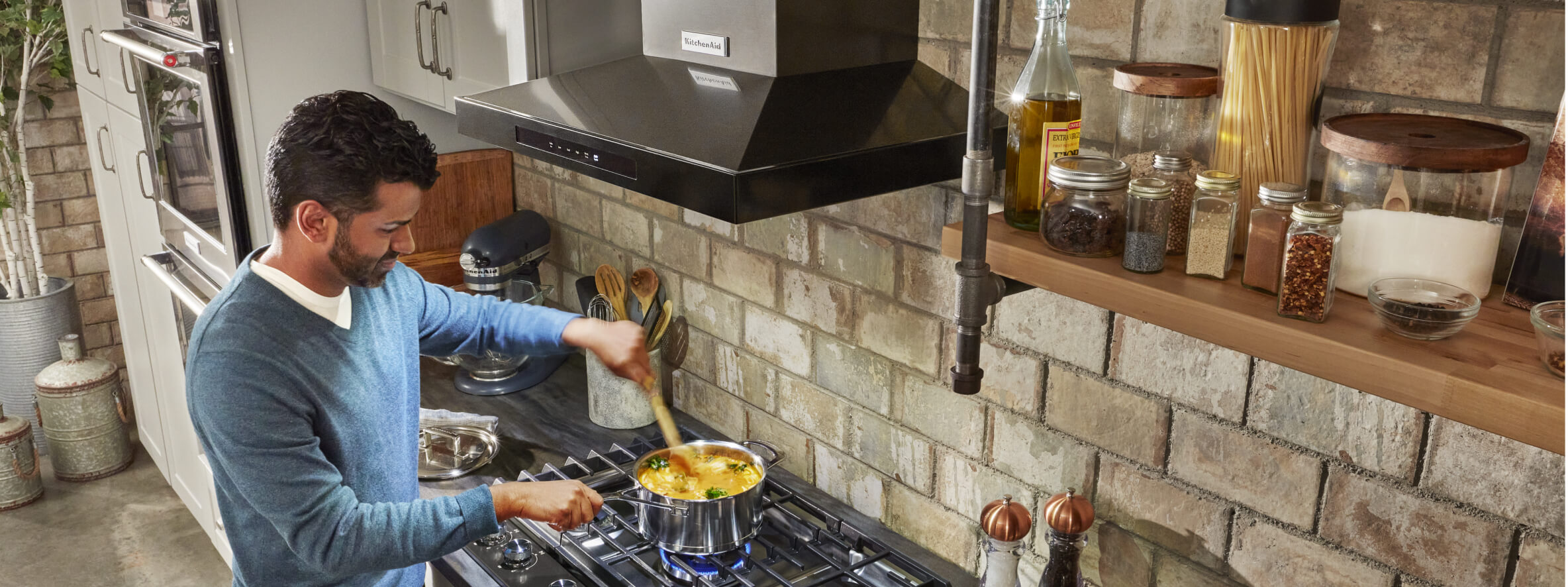 Person stirring food on a range with a KitchenAid® hood above it