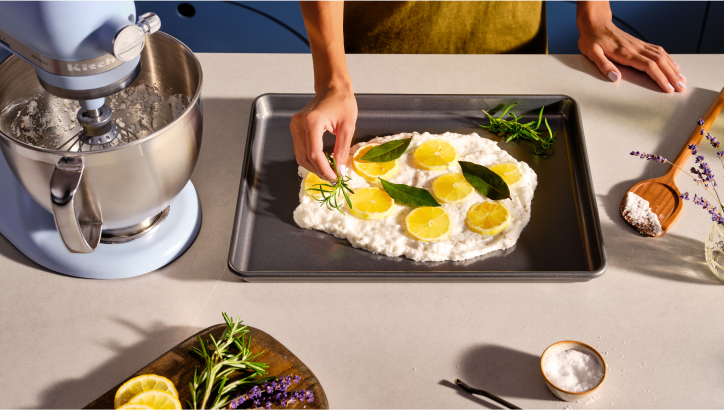 A person adding fresh herbs to a ricotta board with lemon slices and bay leaves.