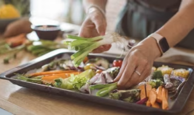 A person adding vegetables to a baking tray.