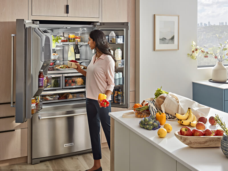 A woman putting produce into her refrigerator