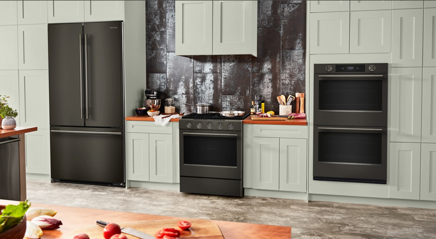 Suite of KitchenAid® Black Ore appliances in light sage green cabinetry